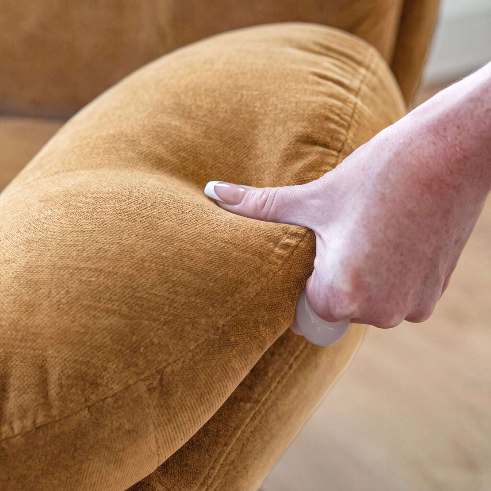 Main pressant le dossier du fauteuil Ricci pour montrer le moelleux du garnissage en velours jaune moutarde