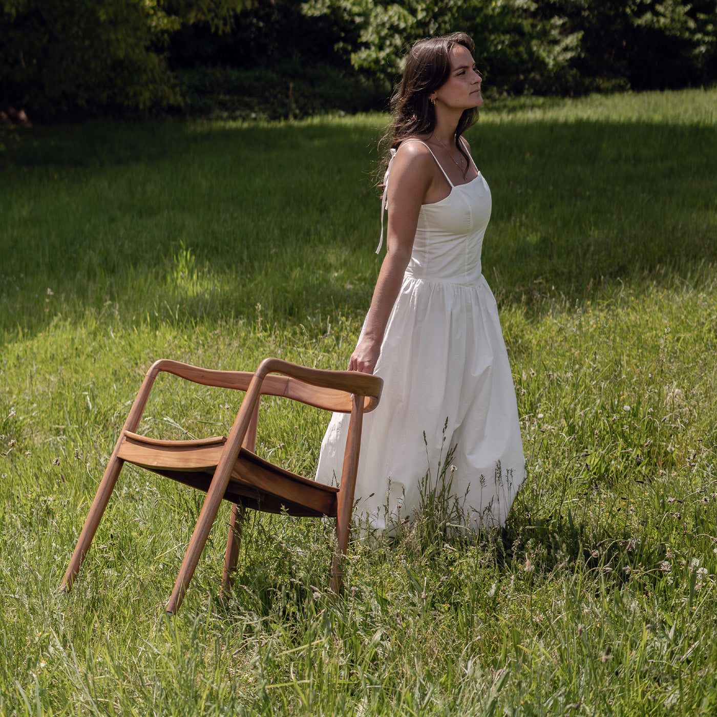 Chaise design en bois massif style scandinave tenue par une femme en robe blanche dans un jardin ensoleillé – Maison Pavane