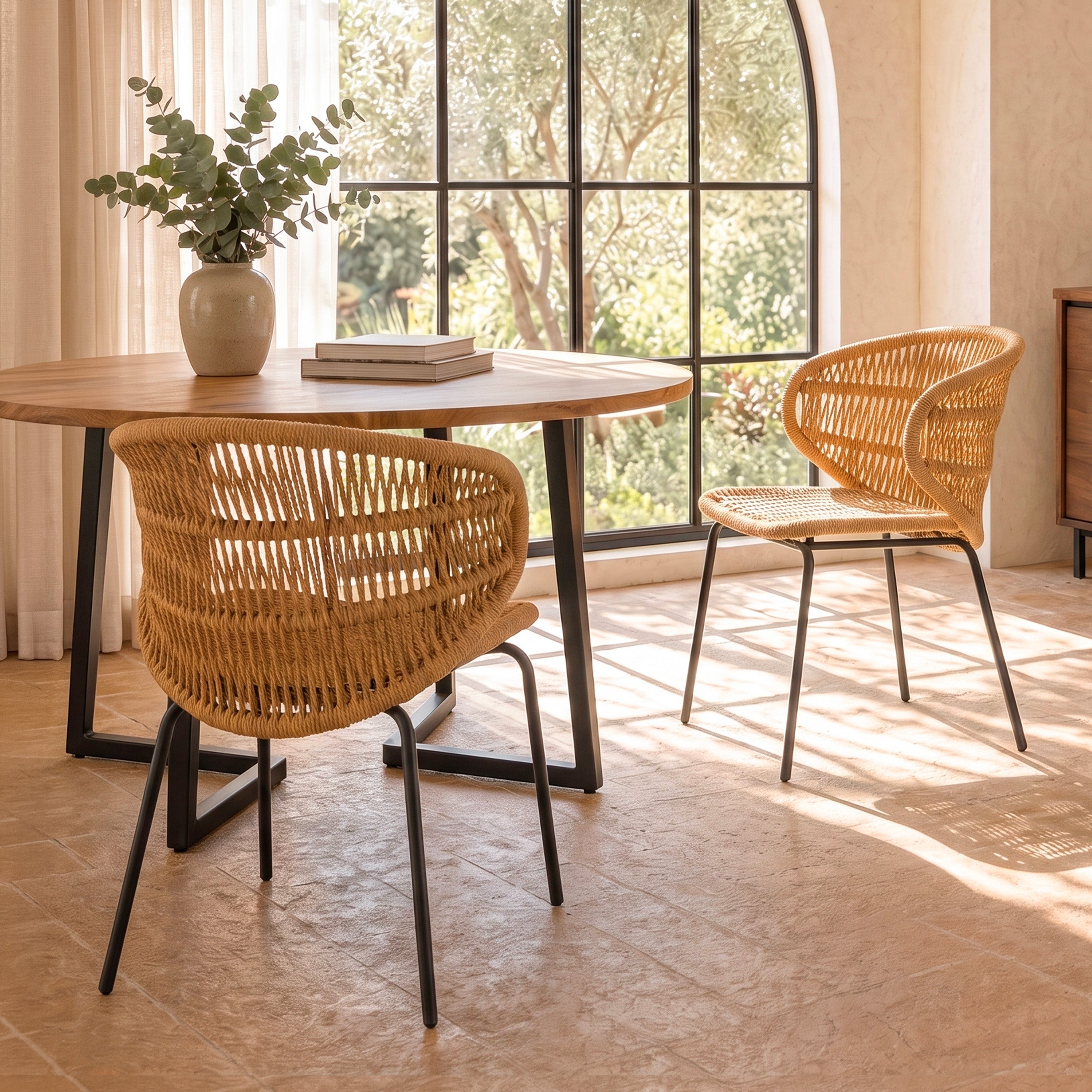 Deux chaises Lara Maison Pavane en rotin tressé, intérieur/extérieur, autour d'une table ronde en bois.