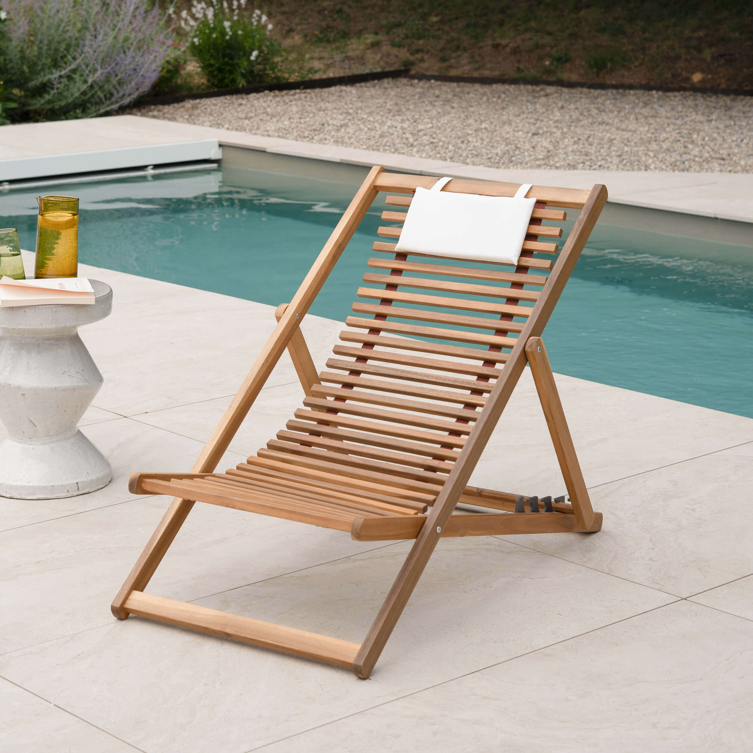 Transat pliant en bois d'acacia avec appuie-tête blanc au bord d'une piscine, ambiance estivale lumineuse – Maison Pavane