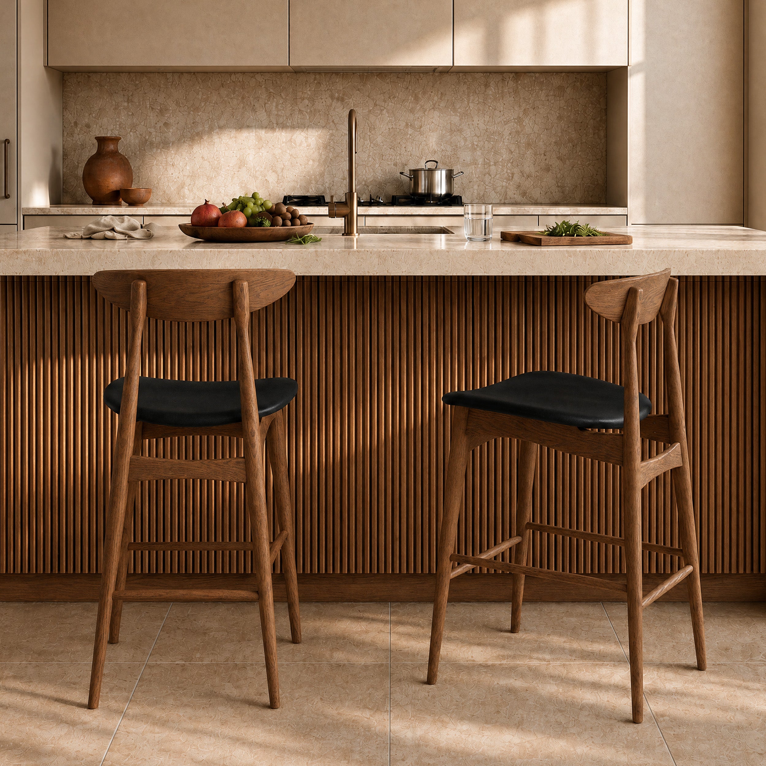 Lot de 2 chaises de bar Josette en bois d'hévéa et assise cuir synthétique noir, vues de dos devant un îlot central en travertin