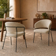 Lot de 2 chaises Amaya en tissu bouclette beige et pieds en métal noir, autour d'une table ronde en bois dans une salle à manger au sol terrazzo
