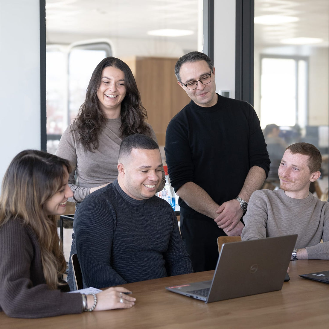 Équipe Service Client souriante en réunion autour d'une table en bois dans un bureau moderne lumineux – Maison Pavane