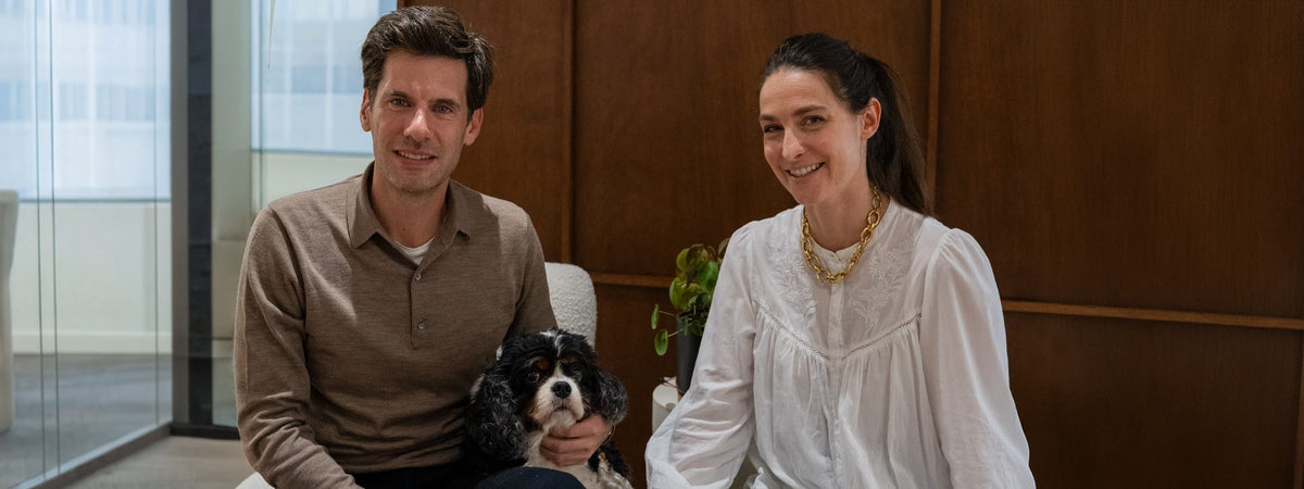 Fondateurs de Maison Pavane souriants avec leur chien, ambiance chaleureuse bois foncé et lumière naturelle – Maison Pavane