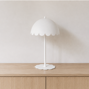 Lampe à poser Flow en métal blanc, éteinte sur un buffet en bois clair devant un mur beige en lumière naturelle