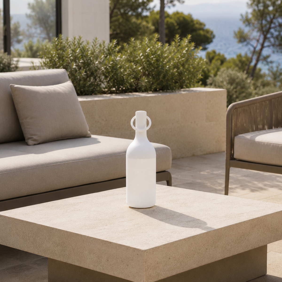 Lampe nomade Elo en plastique blanc, posée sur une table basse en pierre d'une terrasse en bord de mer