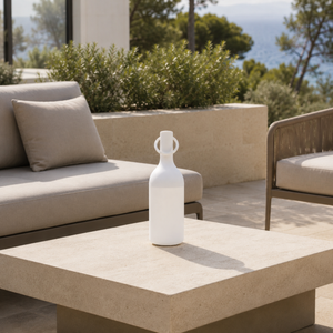 Lampe nomade Elo en plastique blanc, posée sur une table basse en pierre d'une terrasse en bord de mer