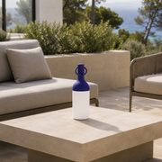 Lampe nomade Elo en plastique bleu, posée sur une table basse en pierre d'une terrasse en bord de mer