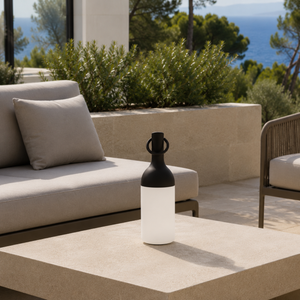 Lampe nomade Elo en plastique noir, posée sur une table basse en pierre d'une terrasse en bord de mer
