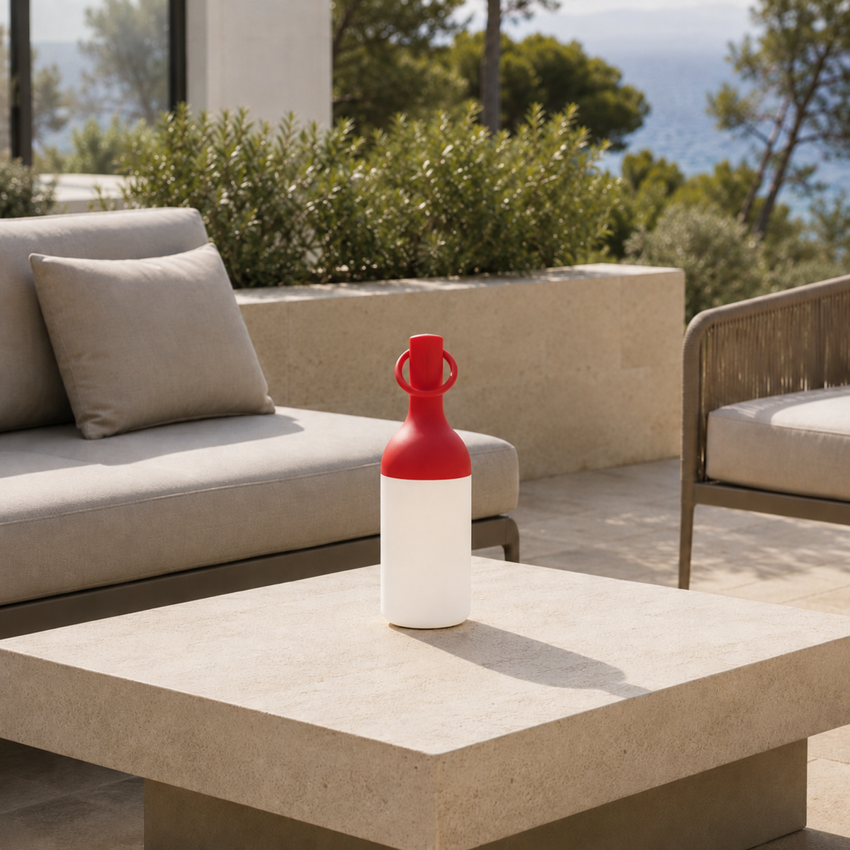 Lampe nomade Elo en plastique rouge, posée sur une table basse en pierre d'une terrasse en bord de mer