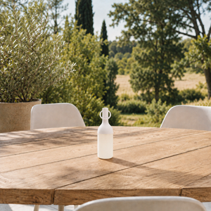 Petite lampe nomade Elo en plastique blanc, posée sur une table en bois d'une terrasse à la campagne