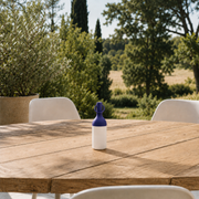 Petite lampe nomade Elo en plastique bleu, posée sur une table en bois d'une terrasse à la campagne