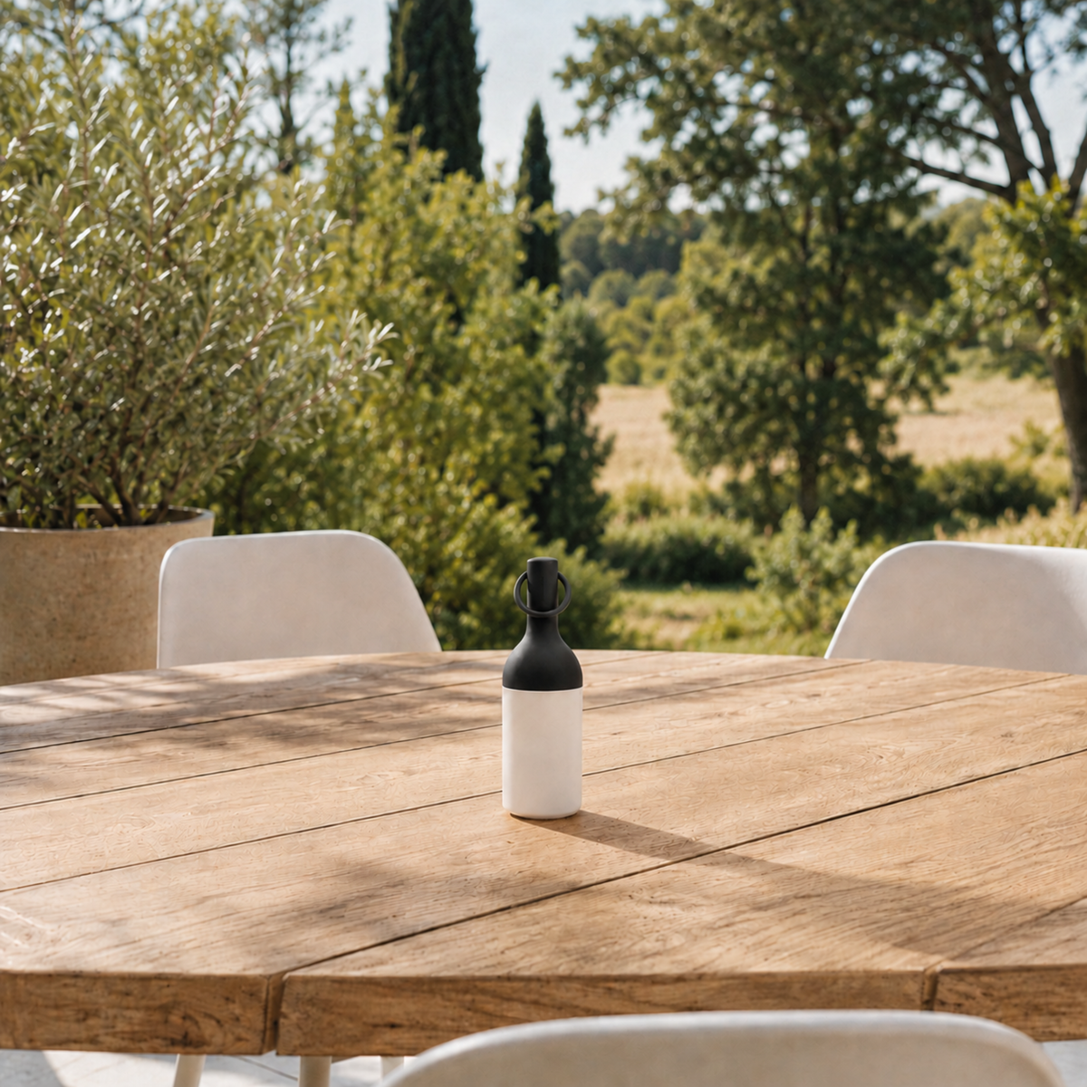 Petite lampe nomade Elo en plastique noir, posée sur une table en bois d'une terrasse à la campagne