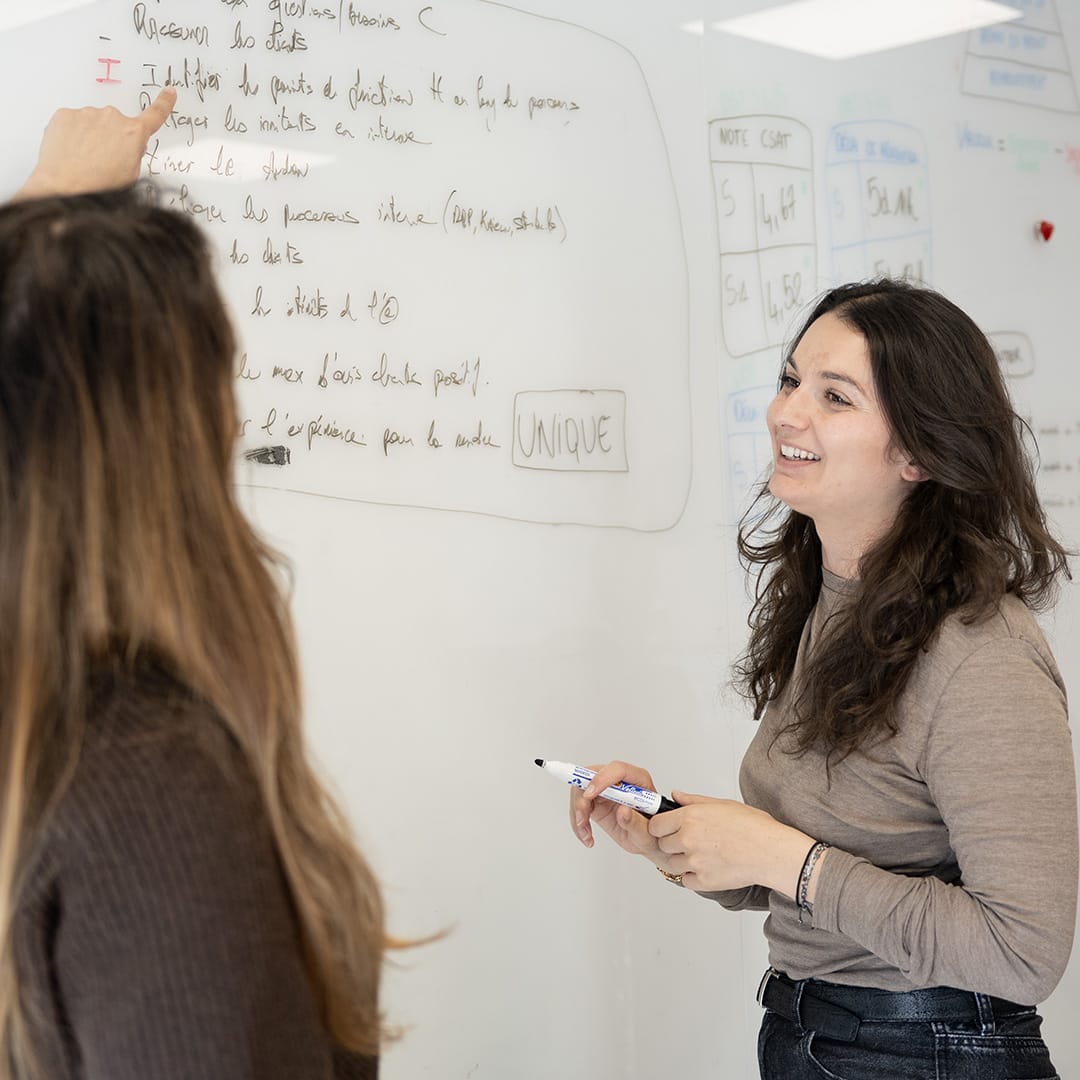 Deux collaboratrices en réunion devant un grand tableau blanc mural dans un bureau lumineux et moderne – Maison Pavane