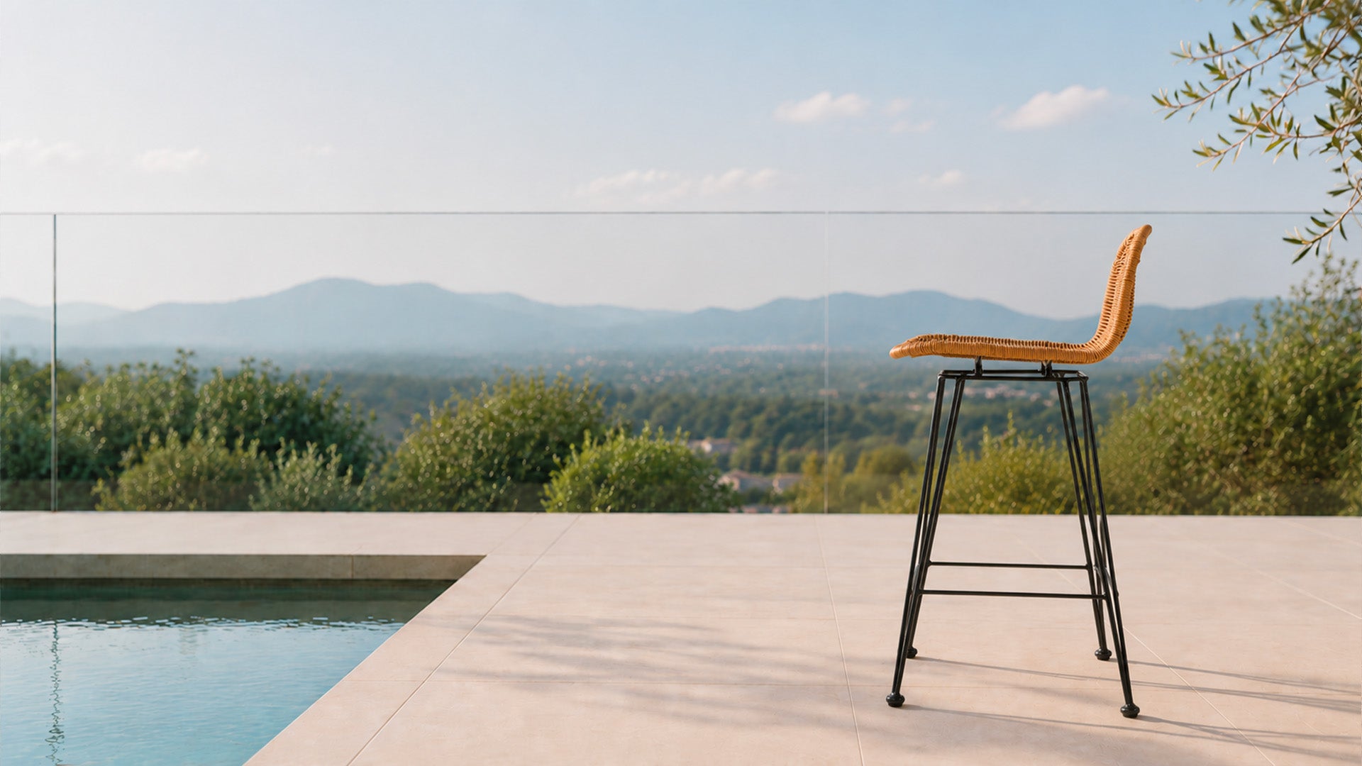 Tabouret de bar en rotin avec pieds en métal noir sur une terrasse avec une piscine en plein été - Maison Pavane